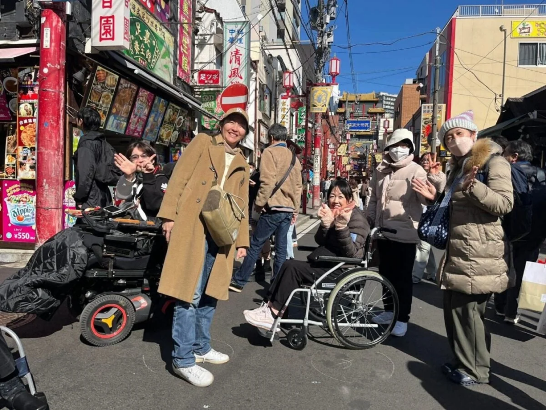 賑やかな中華街のような商店街で、車椅子利用者を含むグループが笑顔でカメラにポーズをとっています