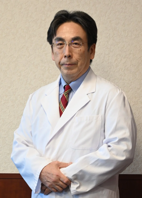 白衣を着用し、眼鏡をかけた中年の男性がカメラをまっすぐ見つめている上半身のポートレート写真です。医療関係者や研究者といった専門家を思わせる落ち着いた雰囲気です。